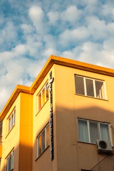 Sunlit building corner with golden hues against a blue sky with fluffy clouds.