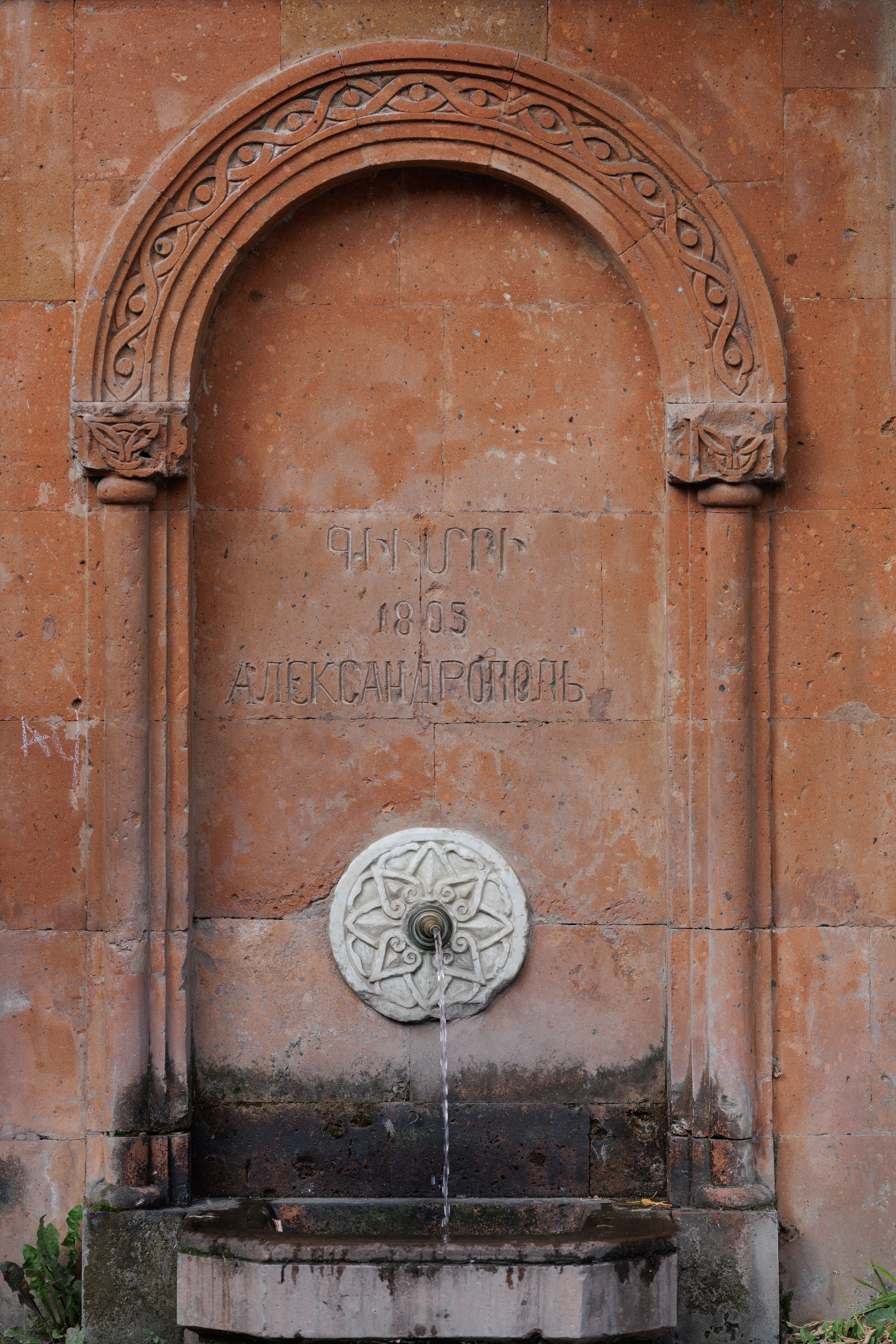 Historic ornate stone fountain with carved arch details and flowing water, perfect for architecture enthusiasts.