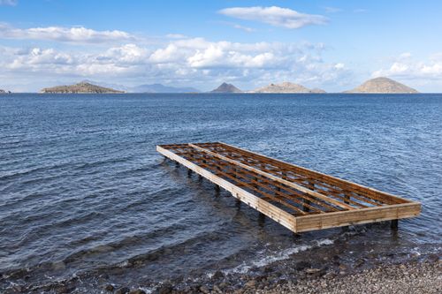 Free Wooden pier extending into the Aegean Sea with distant islands and a blue sky. Stock Photo