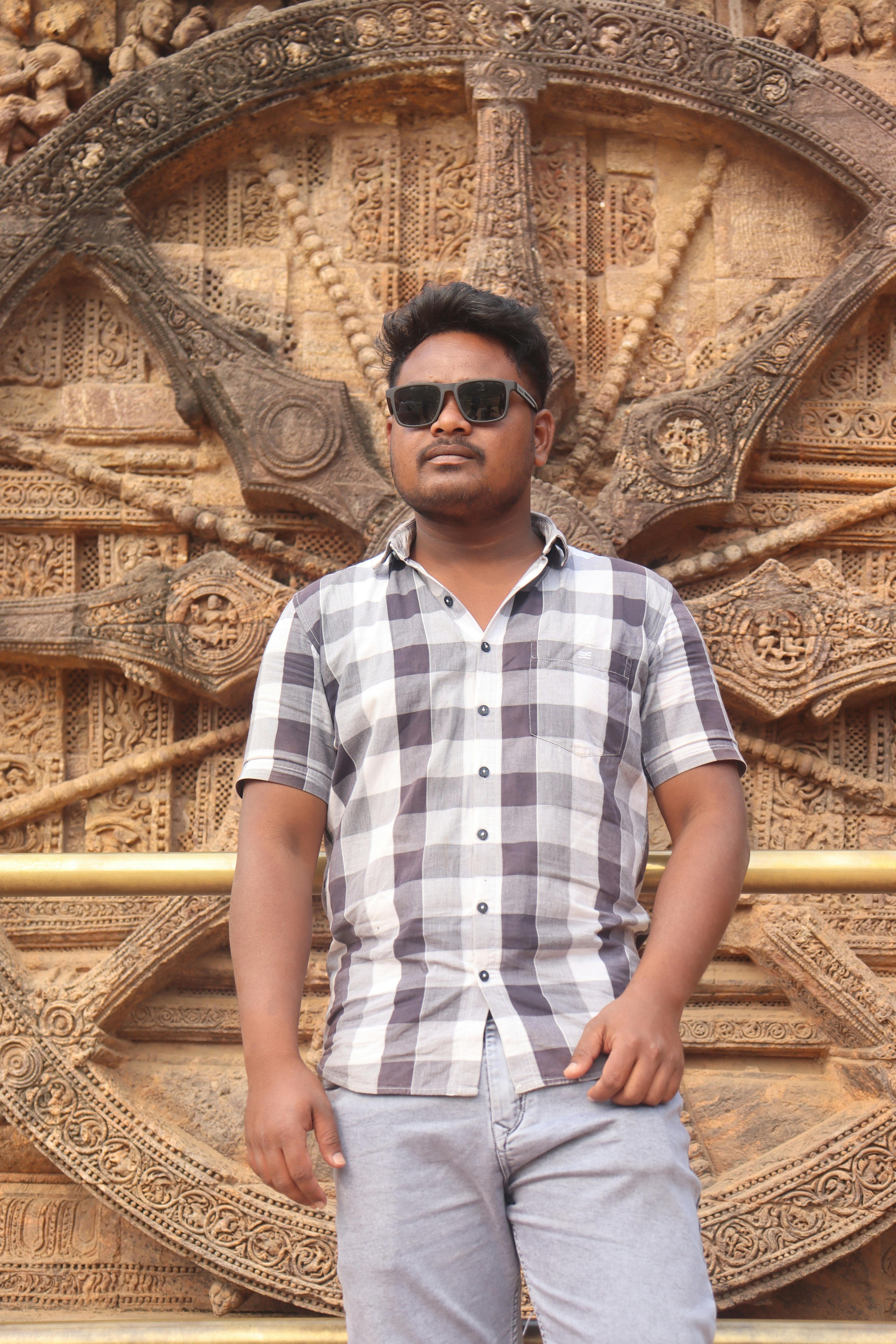 A man poses confidently in front of the intricate stone wheel of Konark Sun Temple, Odisha.
