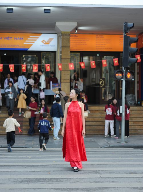 Free A woman wearing a vibrant red dress walks across a bustling street with flags, capturing urban life. Stock Photo