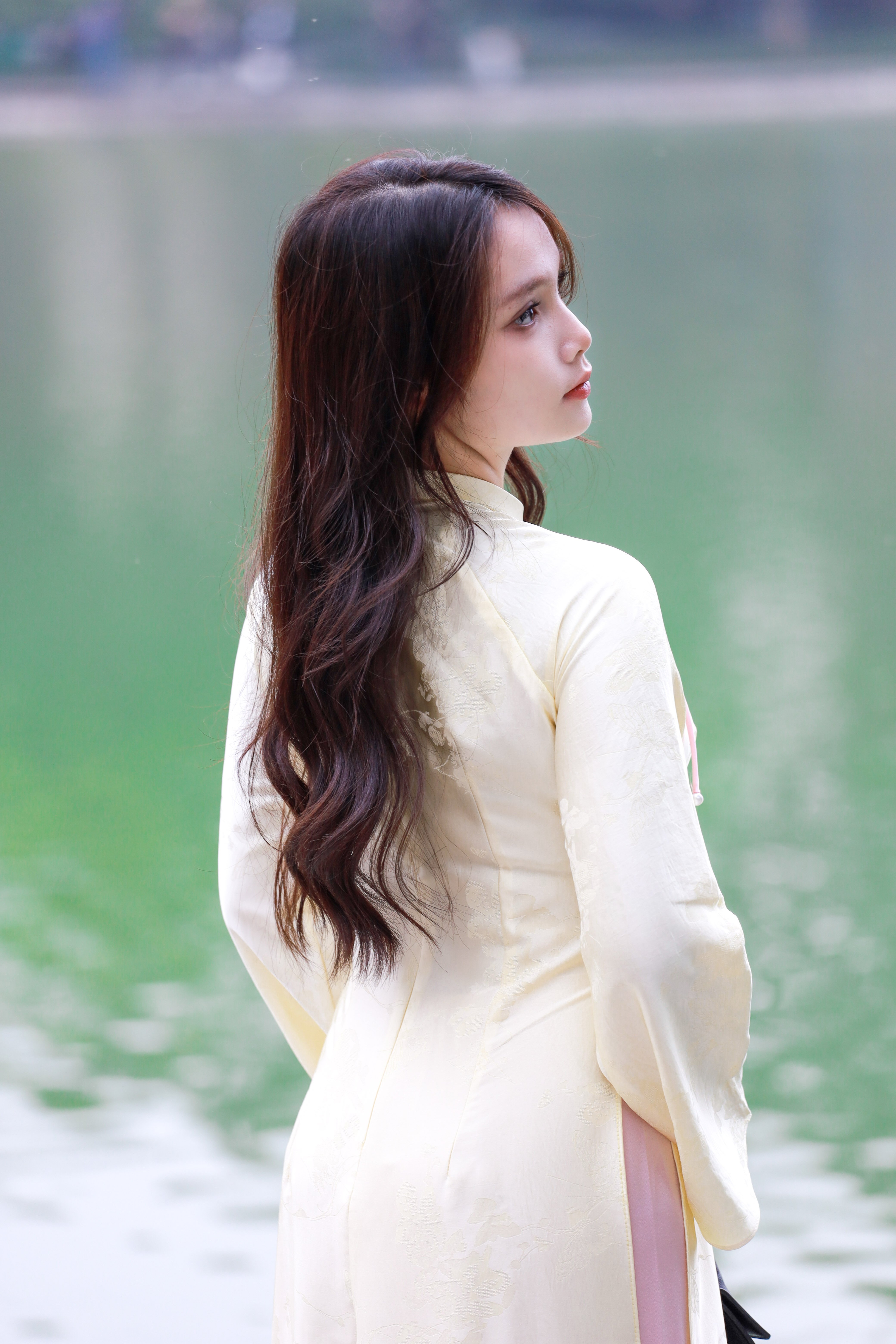 Side view of a woman in a traditional Vietnamese Ao Dai by a serene lake.