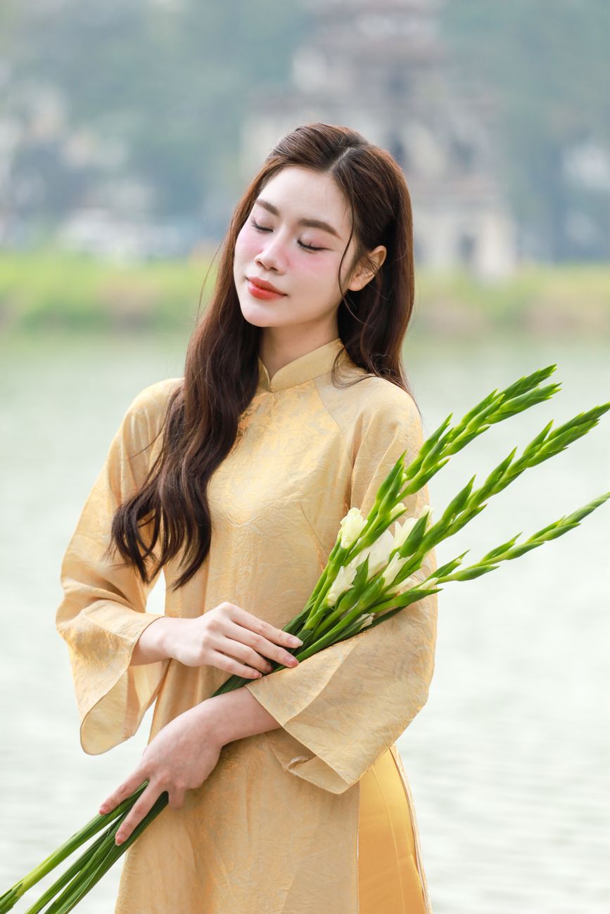 A woman in a traditional dress holds flowers by Hà Nội's Turtle Tower, exuding elegance.