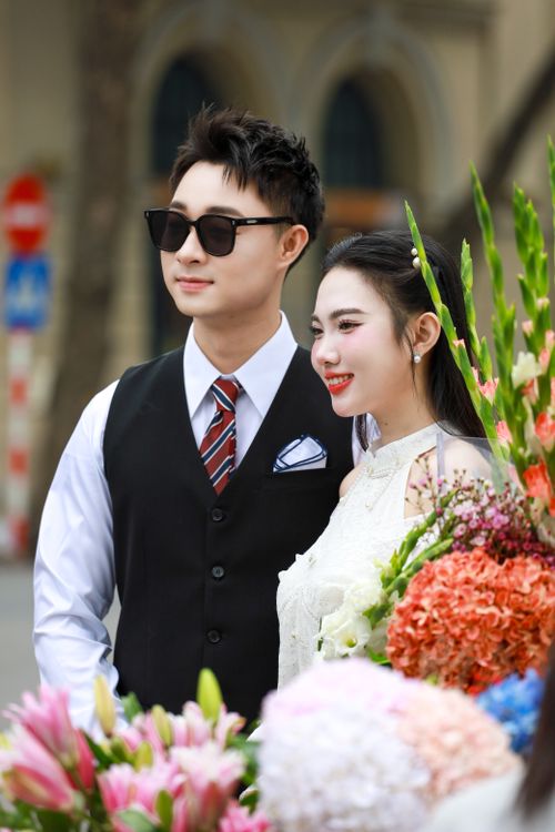 Free Charming couple in wedding attire surrounded by vibrant florals in Hanoi. Stock Photo