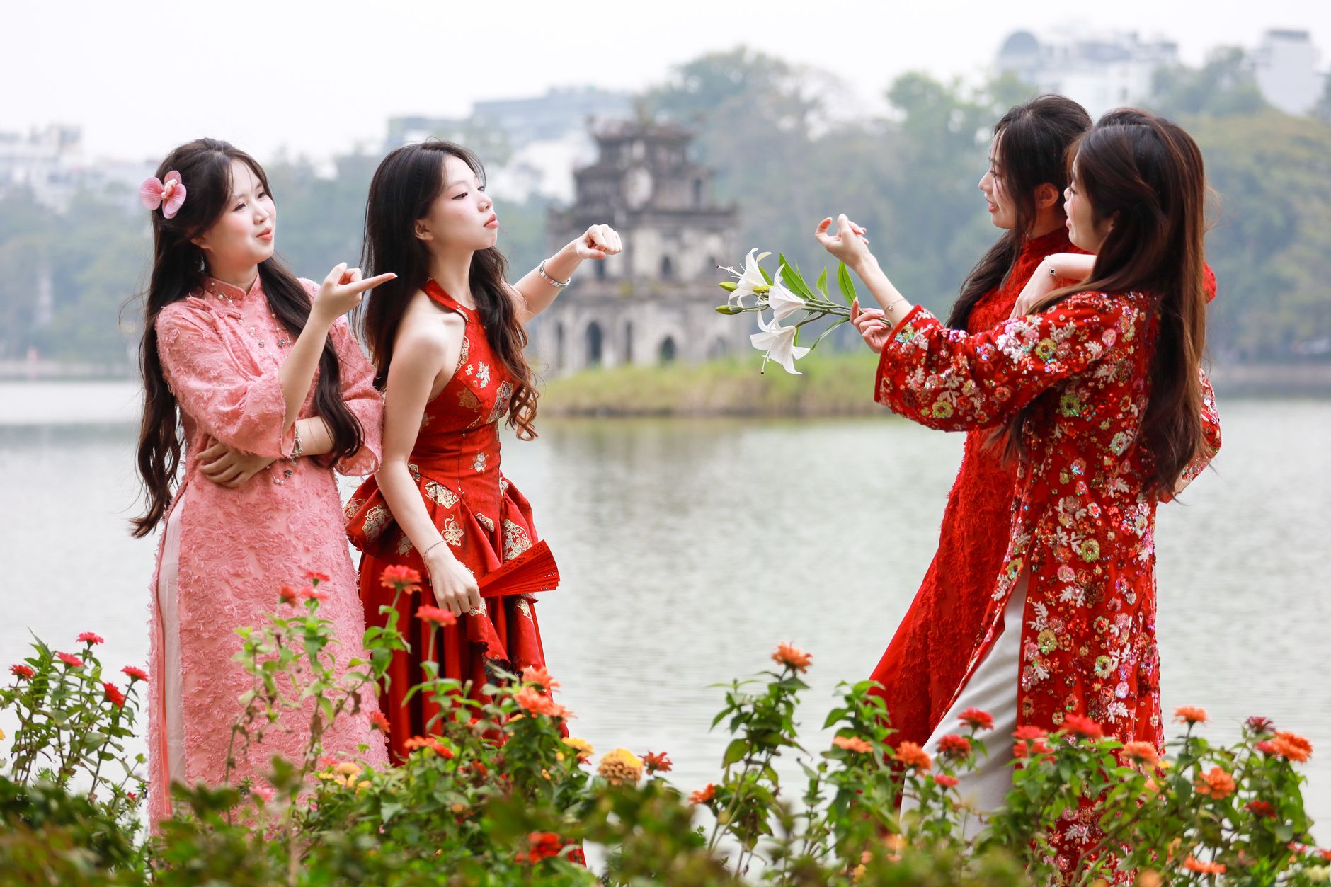 Women in traditional dresses by Hoàn Kiếm Lake, Hanoi, enjoying the scenic view.