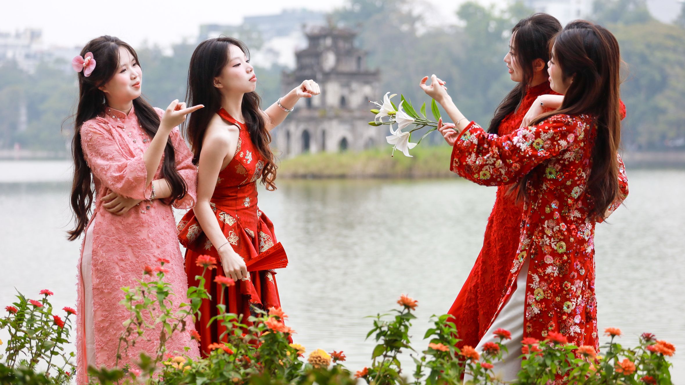 Women in traditional dresses by Hoàn Kiếm Lake, Hanoi, enjoying the scenic view.