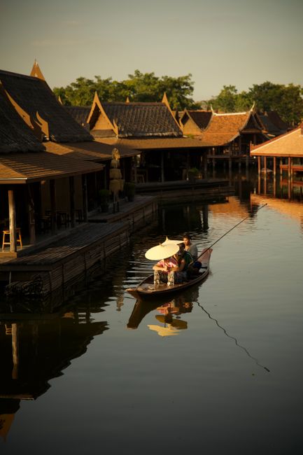 Serene boat ride at sunset through traditional Asian market with wooden architecture and scenic reflections.