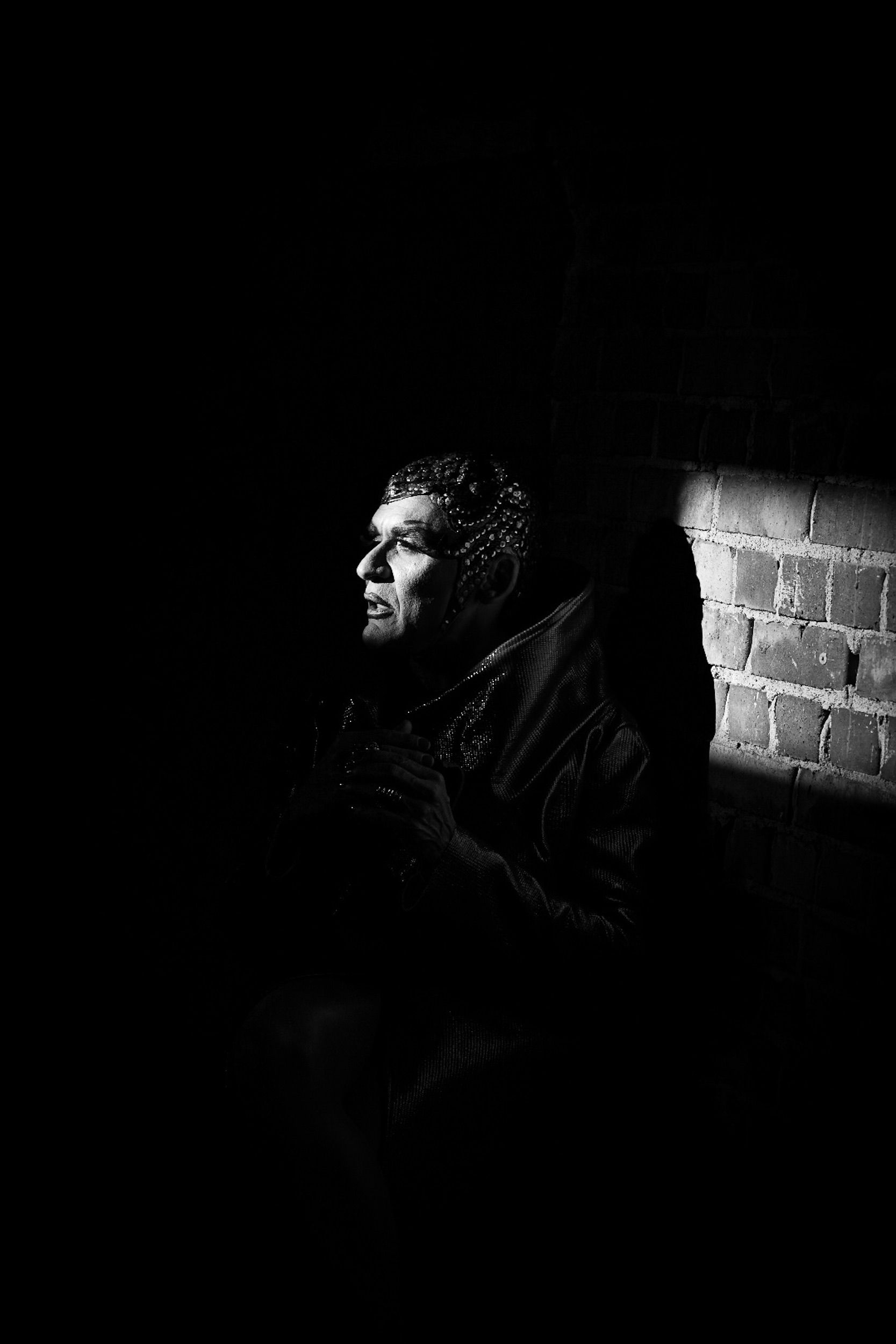 Black and white portrait of a person in shadows against a brick wall.