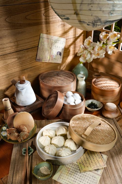Free A cozy setup of traditional Asian steamed buns, bamboo steamers, and tea set in warm lighting. Stock Photo