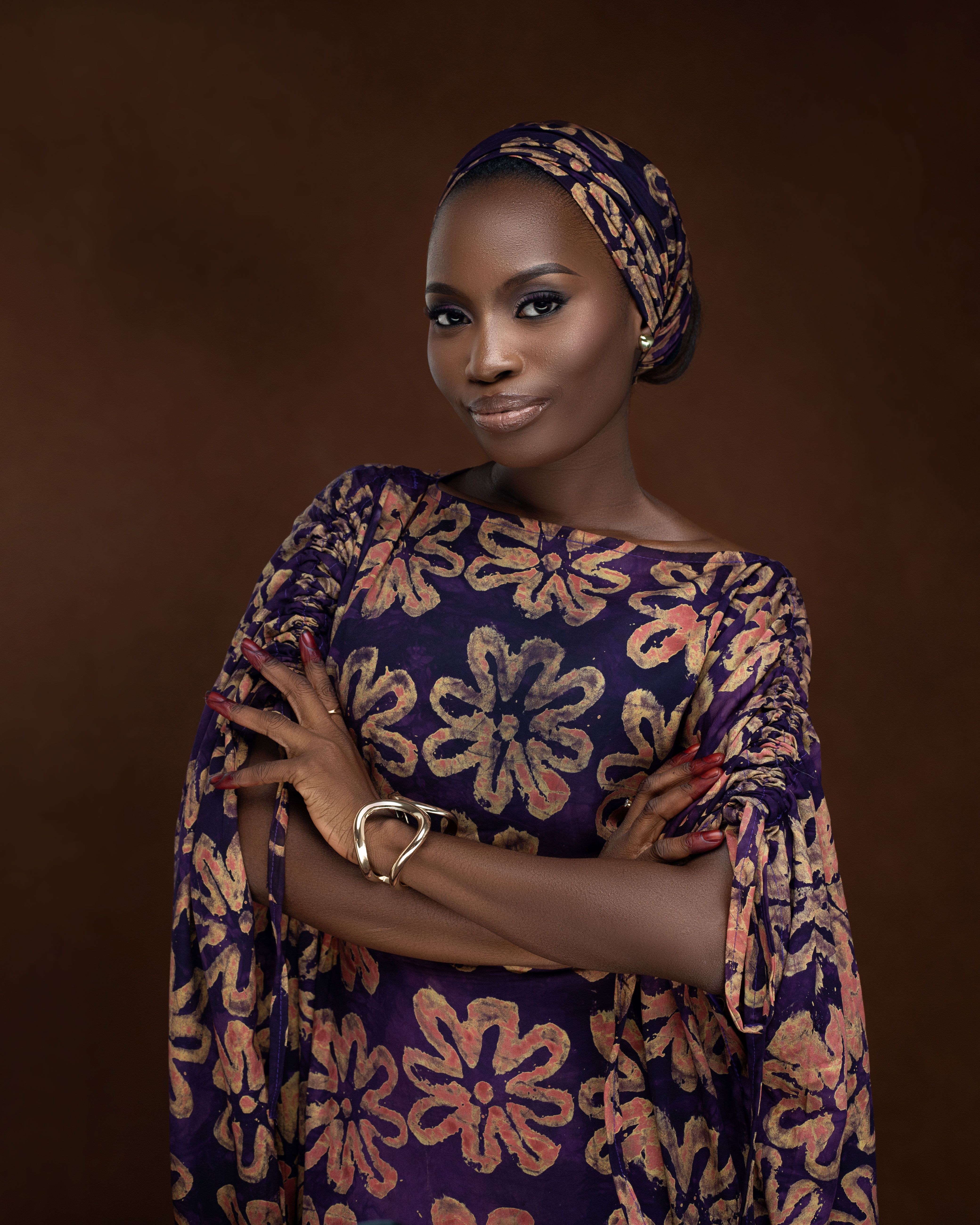 Confident woman wears intricate traditional African dress with floral patterns.