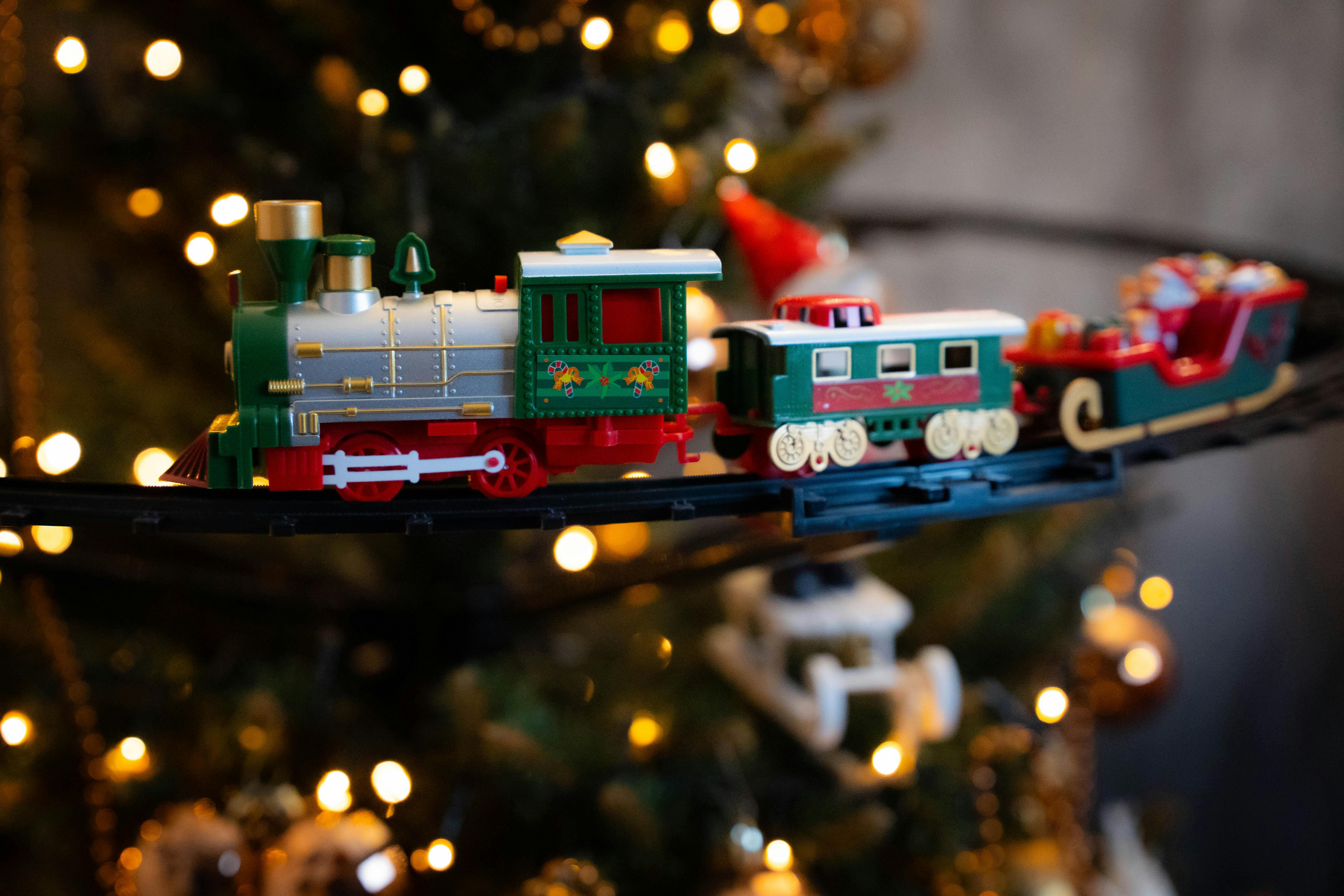 Decorative toy train circling a Christmas tree with glowing lights, creating a festive holiday ambiance.