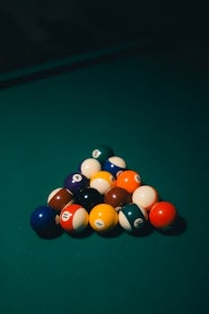 Vibrant billiard balls arranged in a triangle on a dimly lit pool table, ready for play.