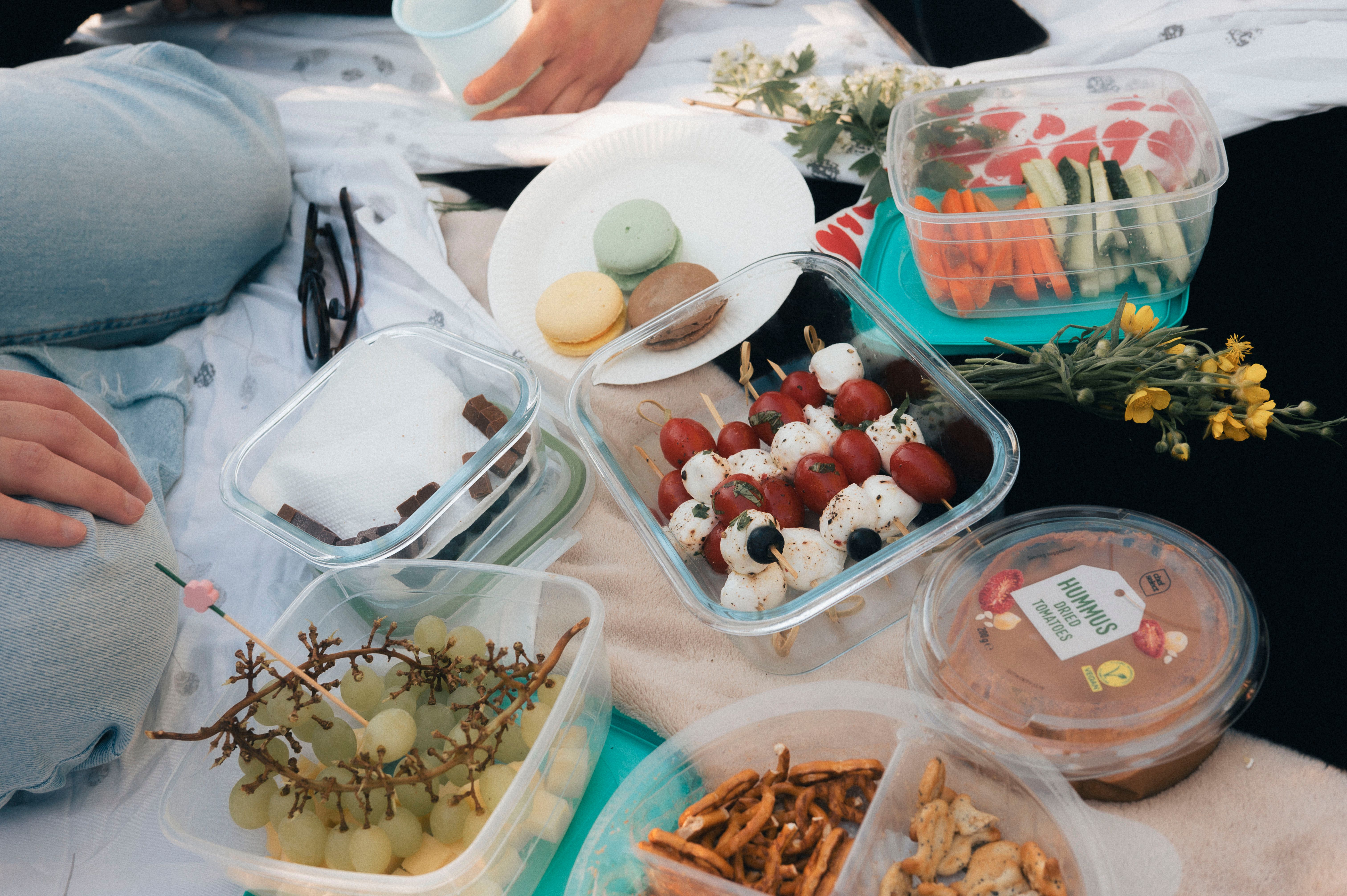 A delightful picnic setup with fresh fruits, vegetables, hummus, and macarons on a sunny day.