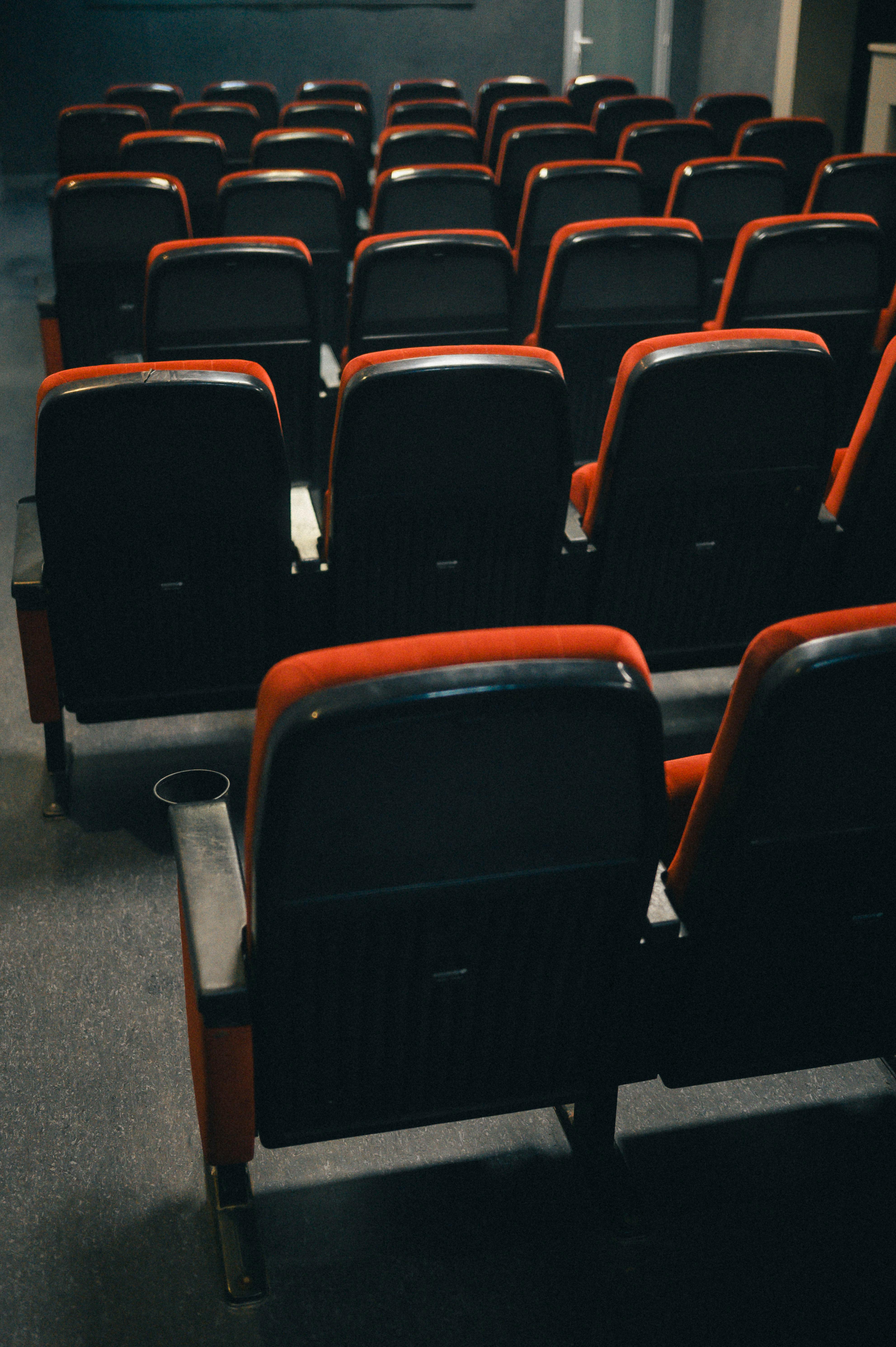 Free Rows of empty theater seats in a dimly lit room, creating a dramatic and nostalgic atmosphere. Stock Photo