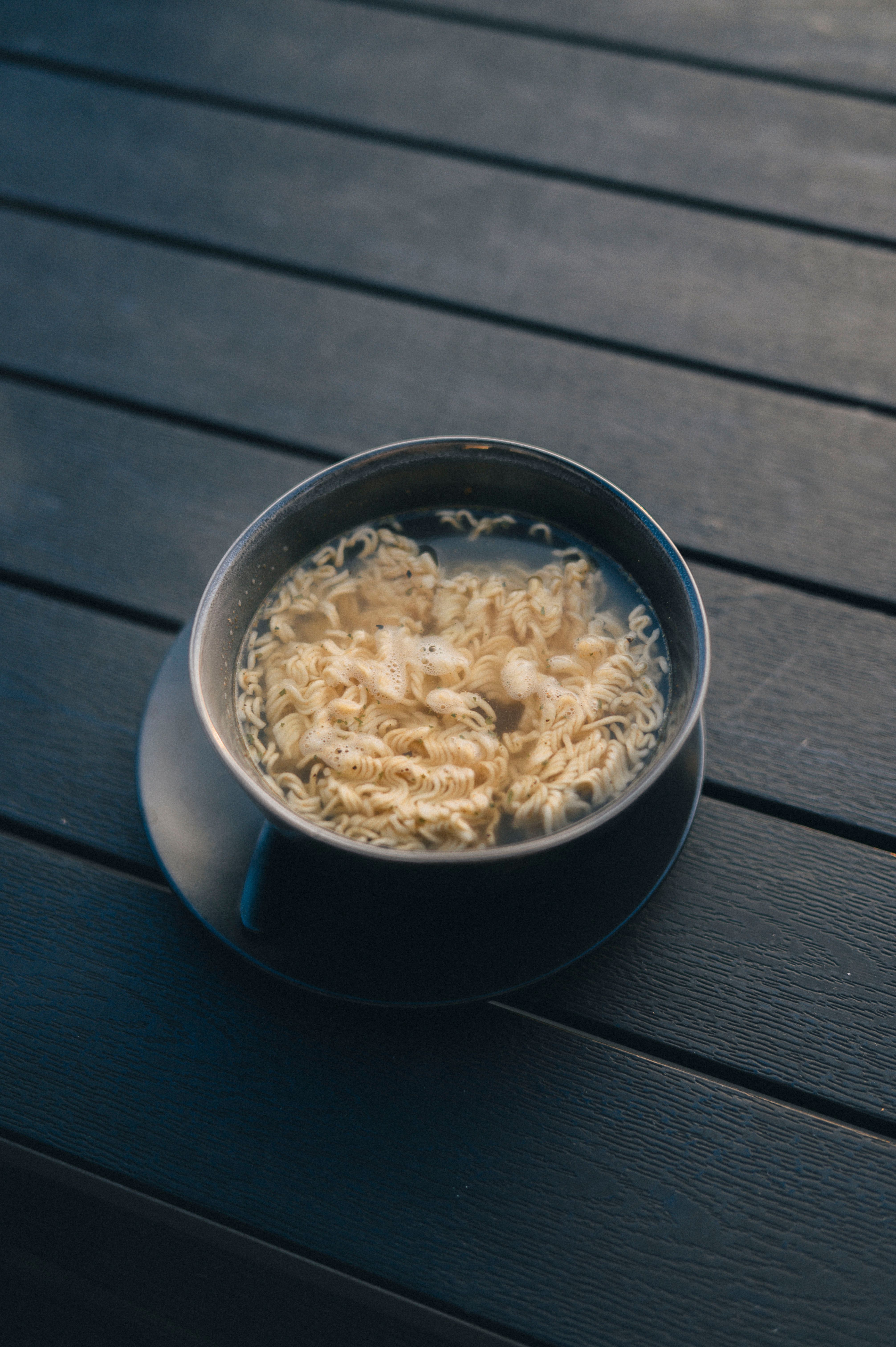A steaming bowl of instant noodles placed on a dark wooden table, creating a cozy vibe.