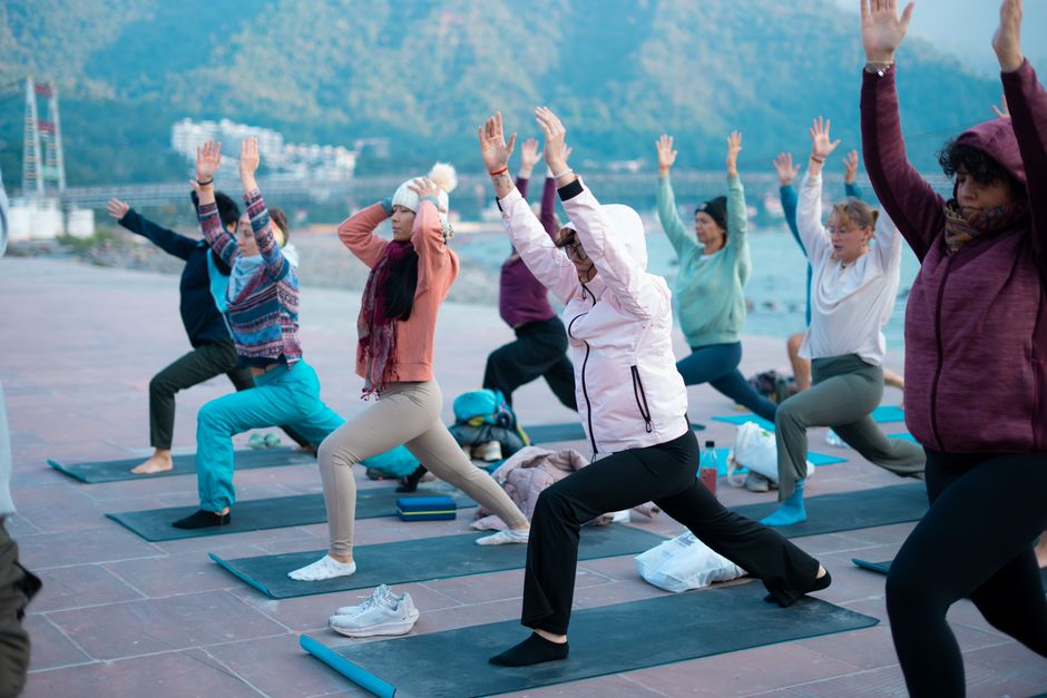 Small group practising a seated yoga pose outdoors on a terrace overlooking Himalayan hills