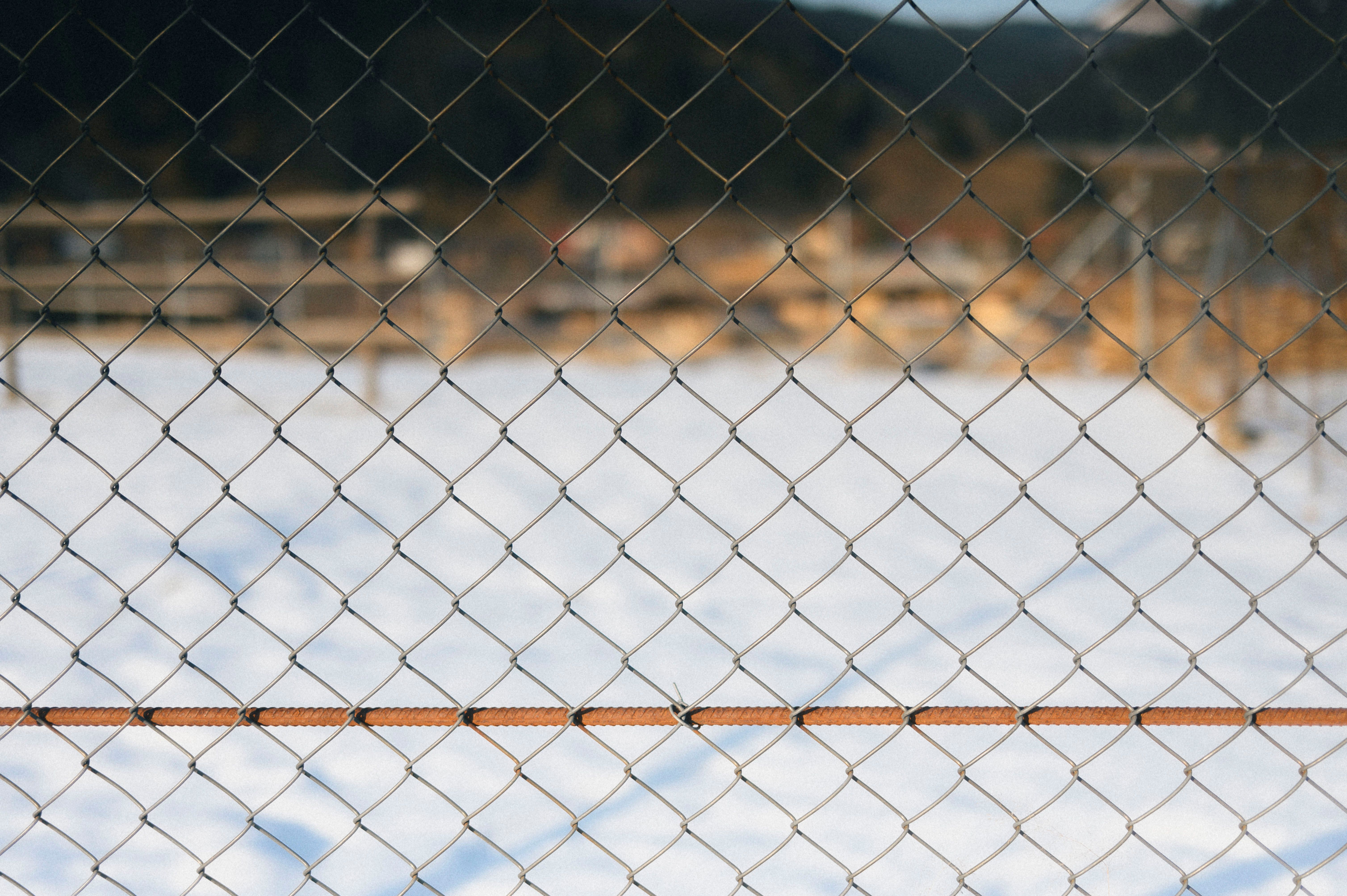 A chain link fence in sharp focus with a soft snowy backdrop, capturing a serene winter scene.