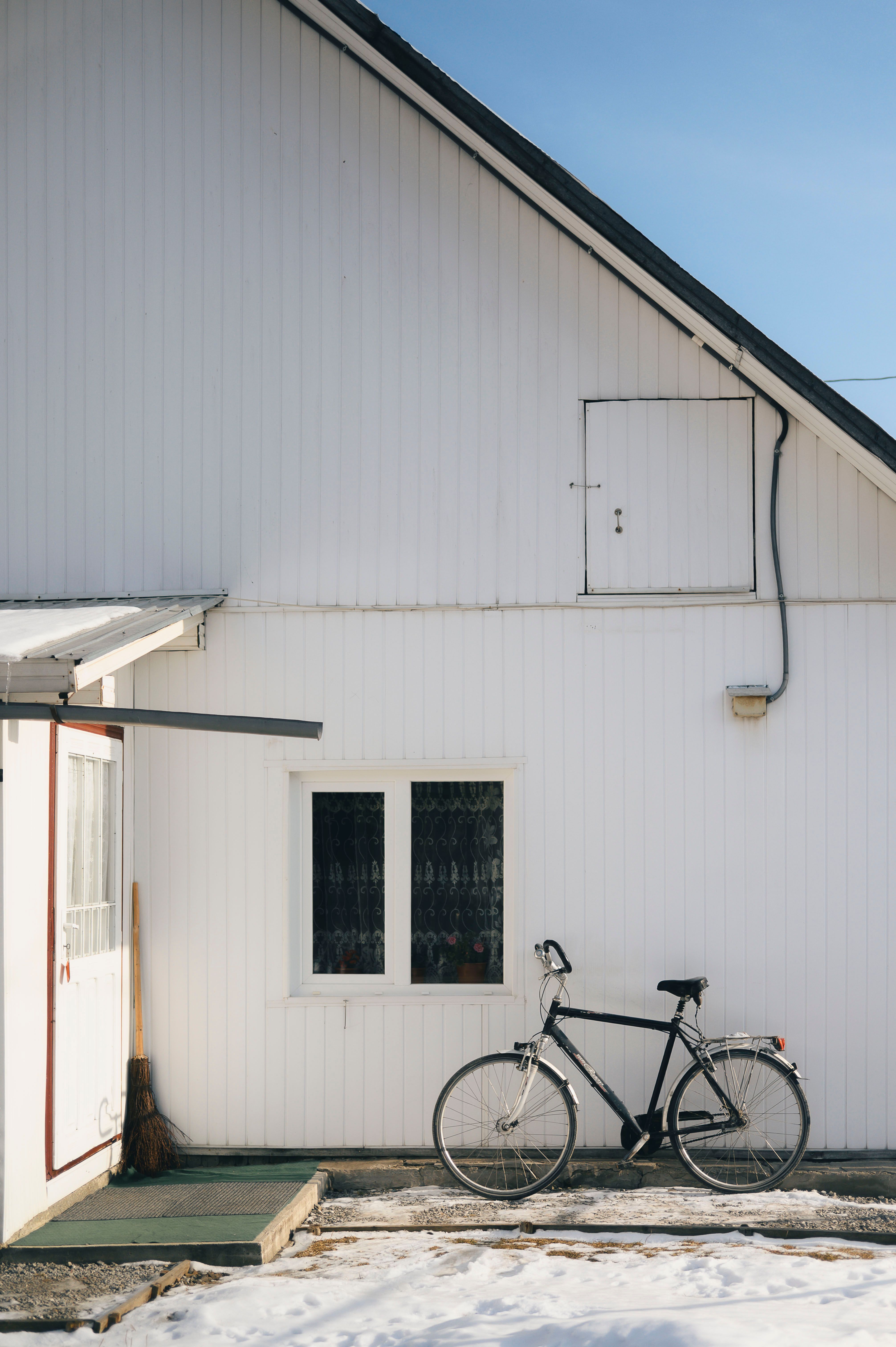 Free A vintage bicycle leaning against a white wooden house with a snowy ground in winter. Stock Photo