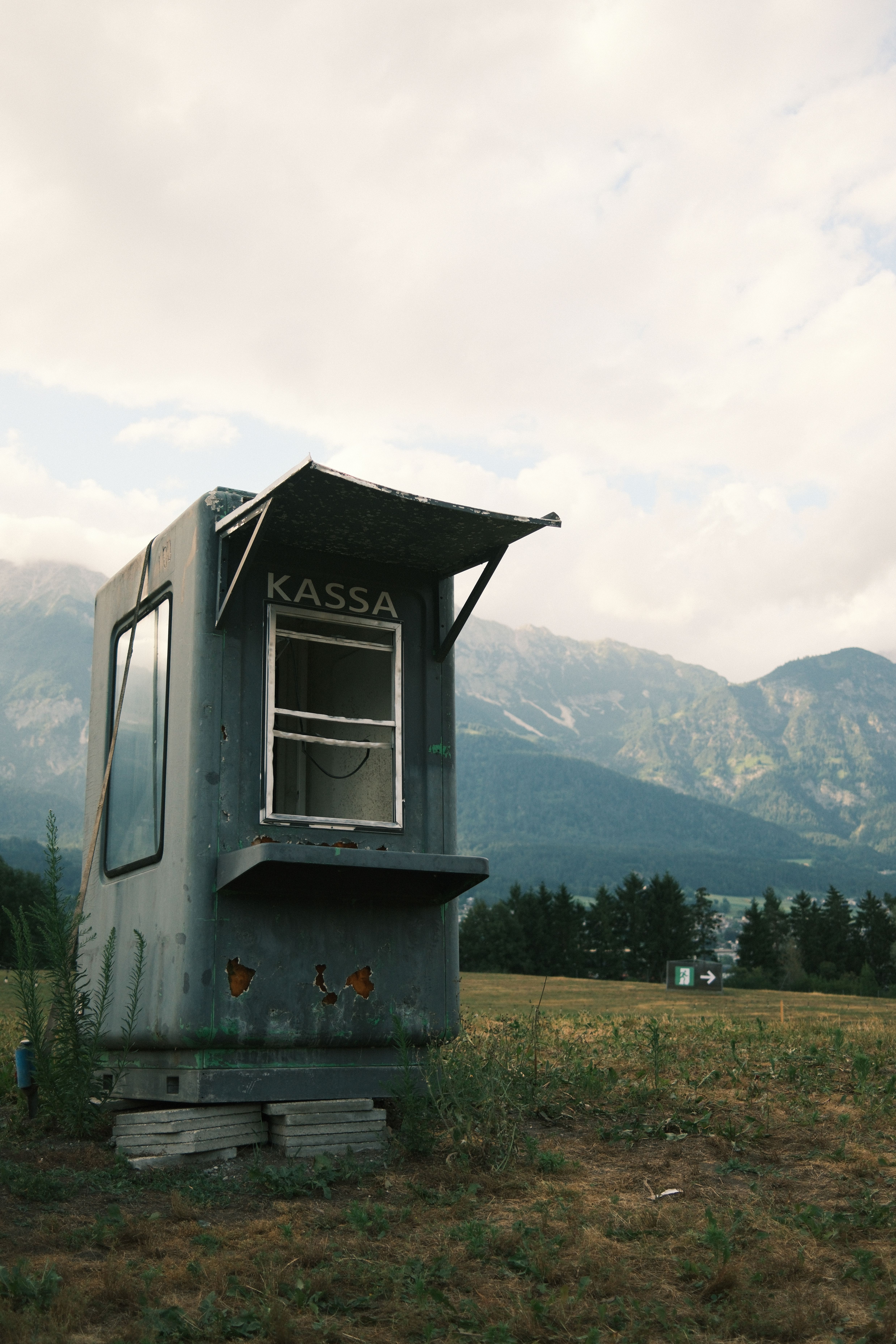 An isolated ticket booth labeled 'Kassa' sits in a scenic alpine field in Innsbruck, Austria.