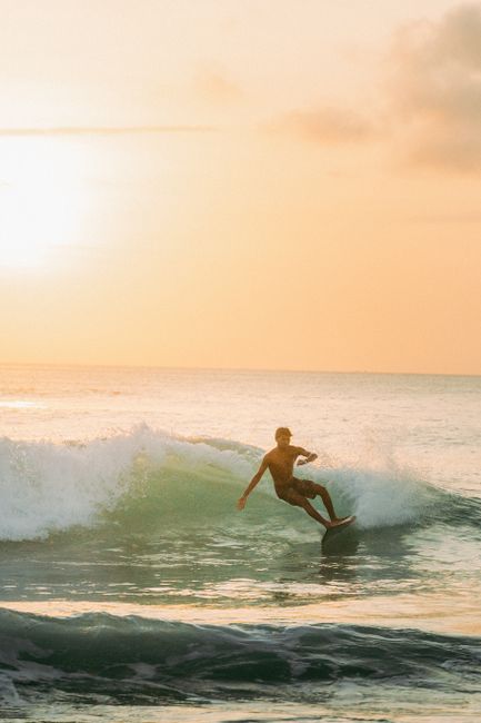 A surfer rides the waves at sunset on a Bali beach, capturing the essence of island adventure.