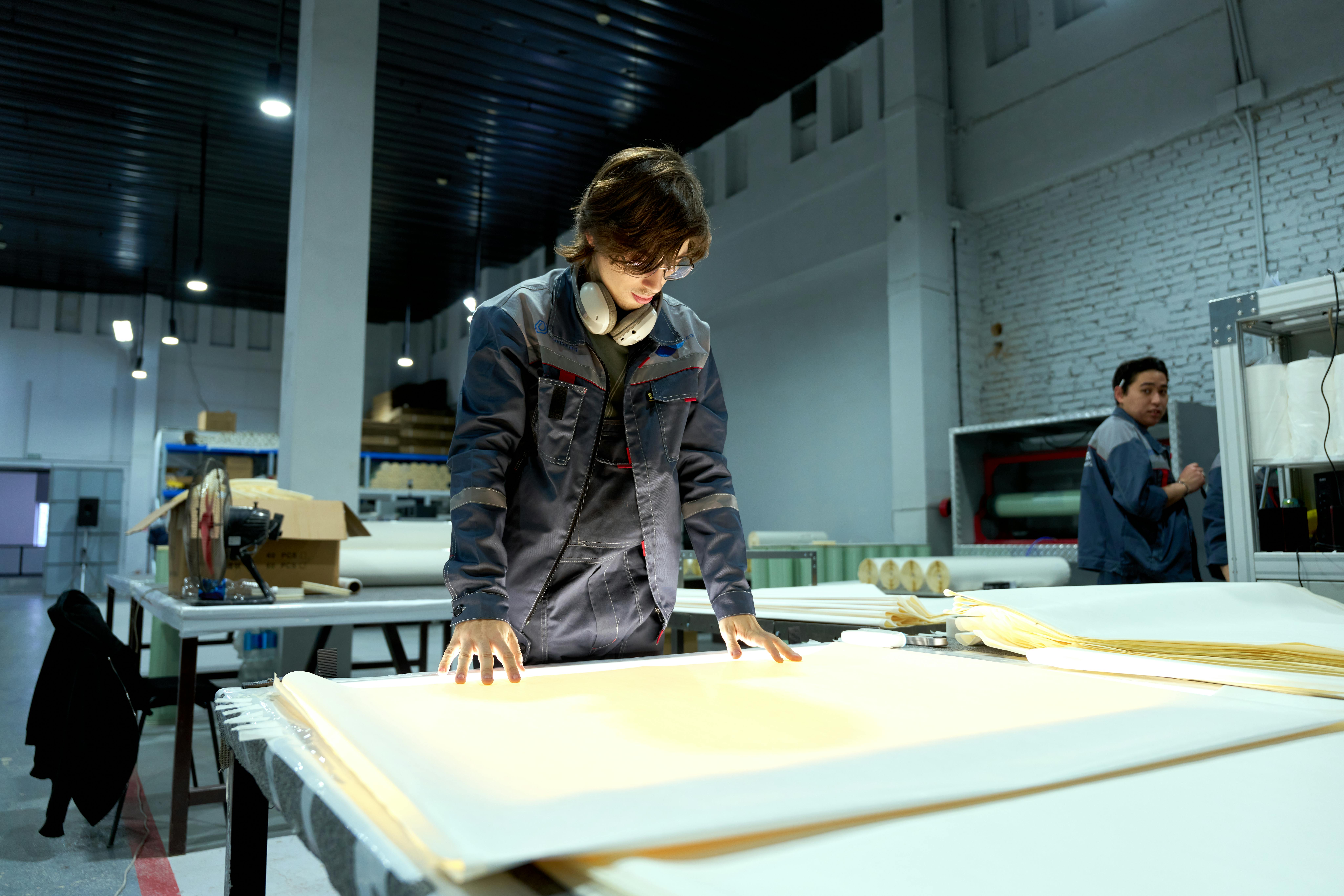 Worker in uniform examining sheets in a brightly lit factory environment, focusing on quality.
