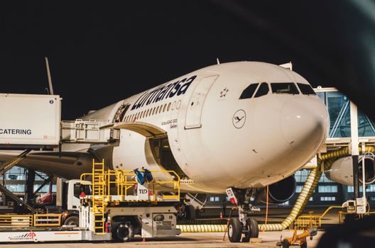 Night view of a Lufthansa airplane docked at an airport terminal with ground services working.