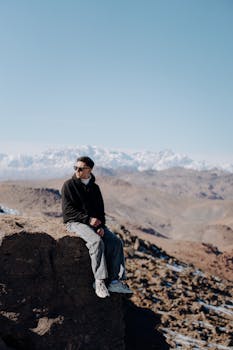 A person sits on a rocky ledge overlooking the Moroccan mountains on a clear winter day.