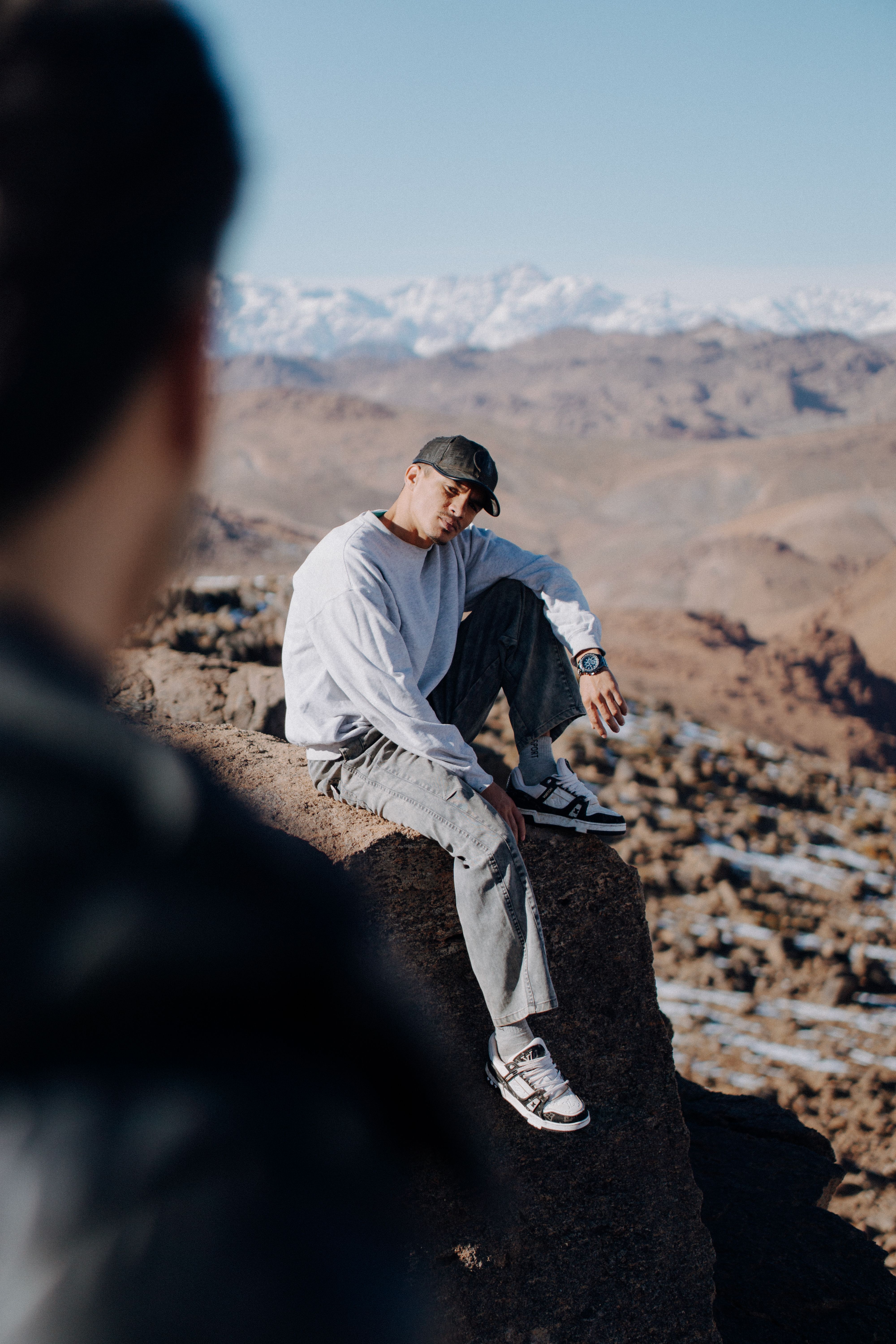 Man sitting on a rock in the Atlas Mountains with snowy peaks in the background.