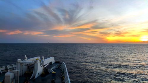 Free Serene ocean view from a ship deck at sunset with vibrant sky colors. Stock Photo