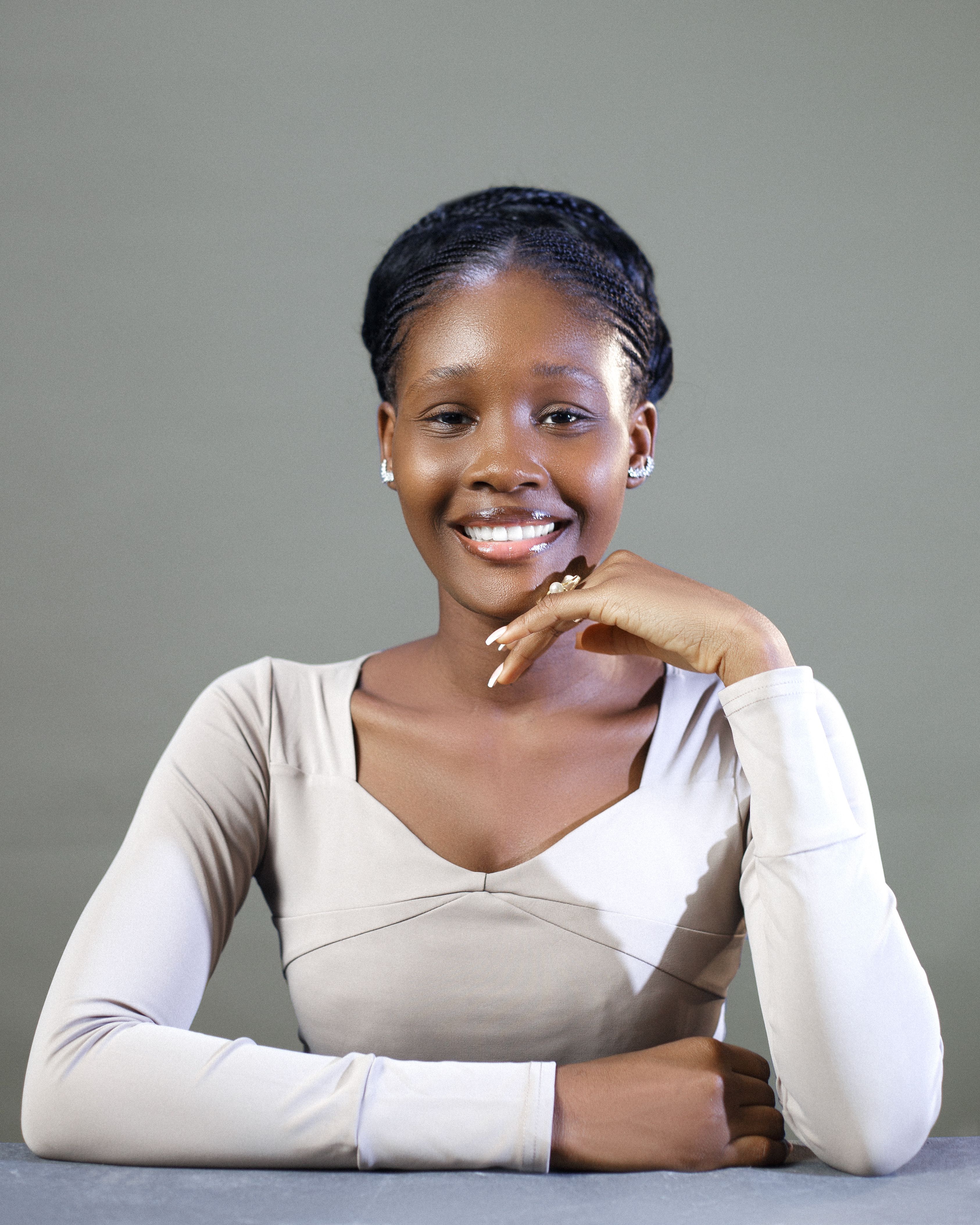 Portrait of a smiling woman sitting against a grey background with a confident expression.