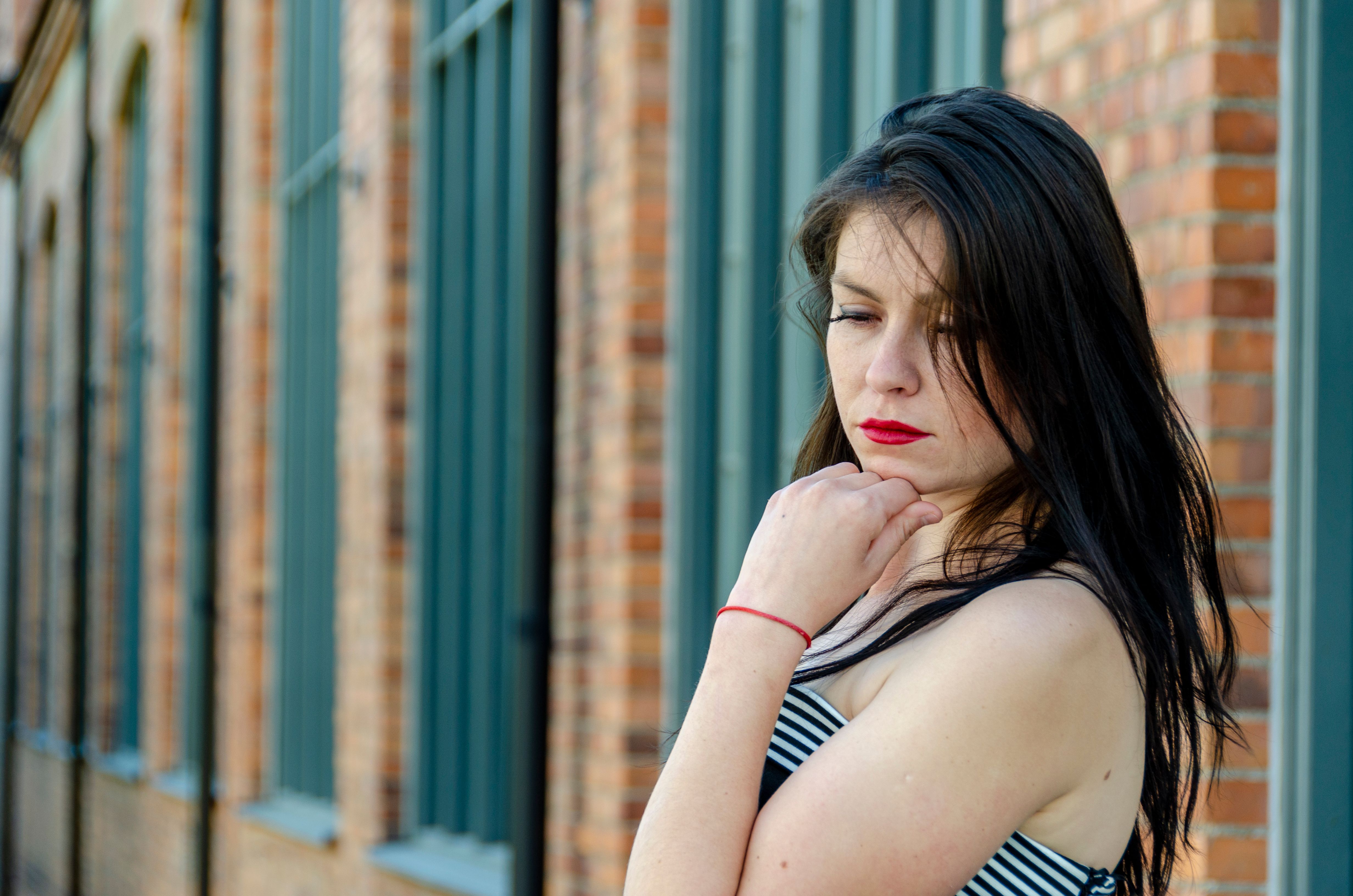 A thoughtful woman in a striped dress stands against a brick building in Stockholm, Sweden.