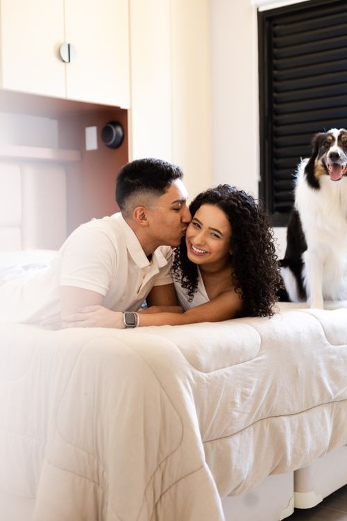Free A young couple shares a tender moment with their pet dog on the bed. Stock Photo