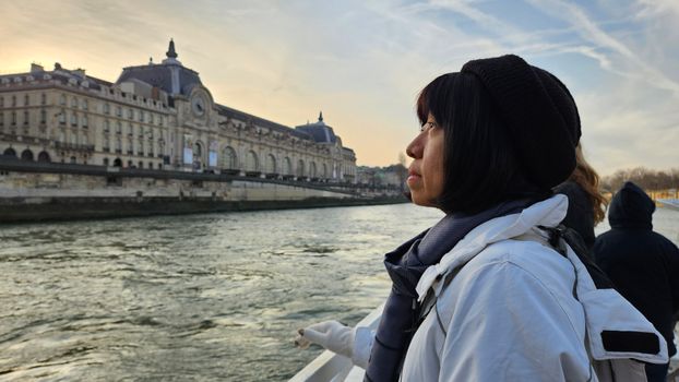A woman enjoys a serene moment by the Seine River with Musée d'Orsay in view.