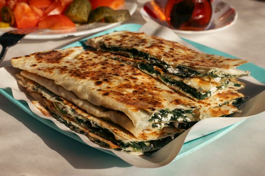 Close-up of freshly made Turkish Gözleme with spinach and cheese on a plate outdoors.