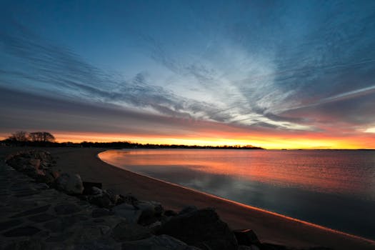 Tranquil sunset over a serene beach with vivid sky colors reflecting on calm waters.