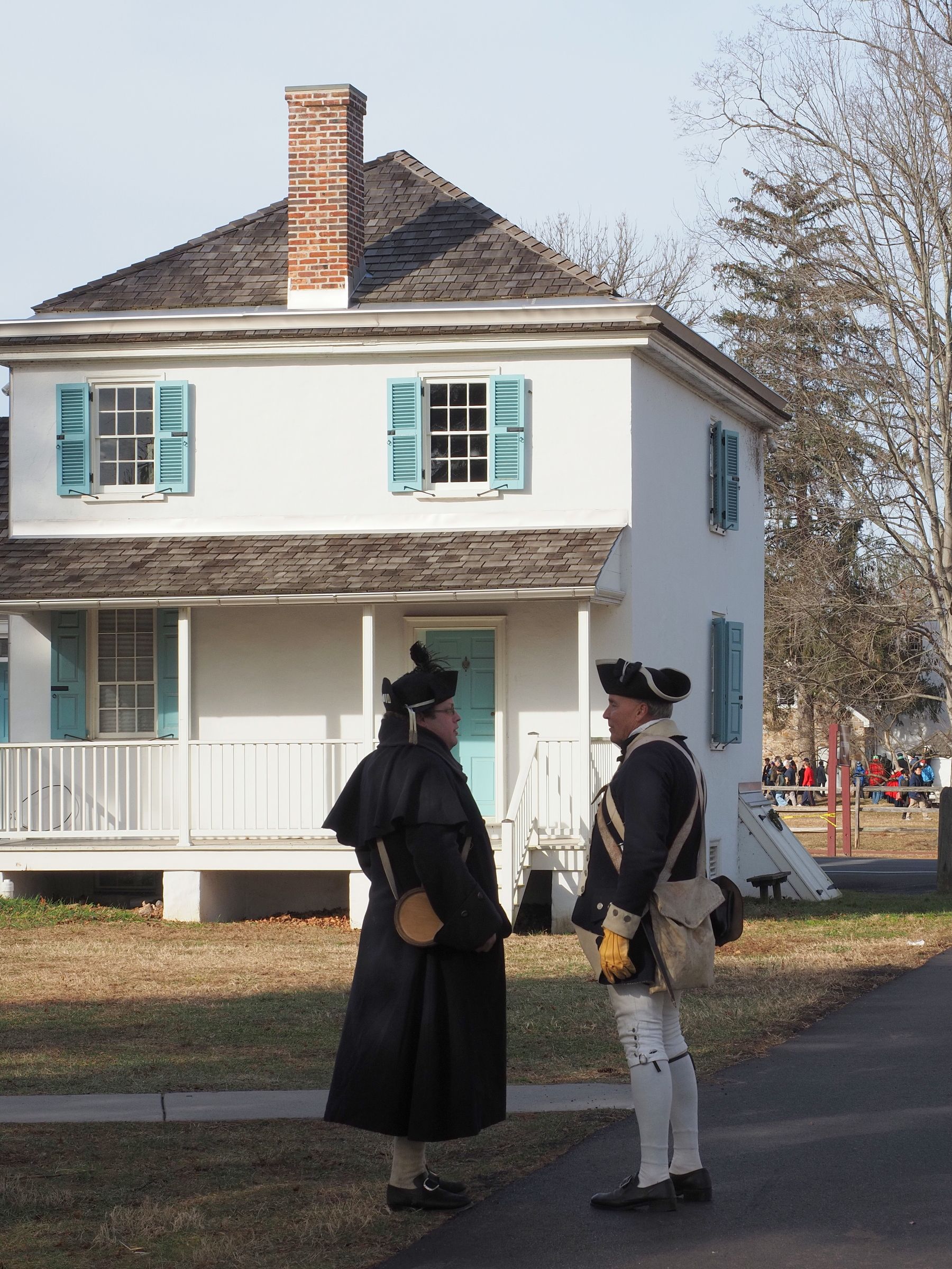 Two historical reenactors in 18th-century attire outside a colonial-style house in Pennsylvania.