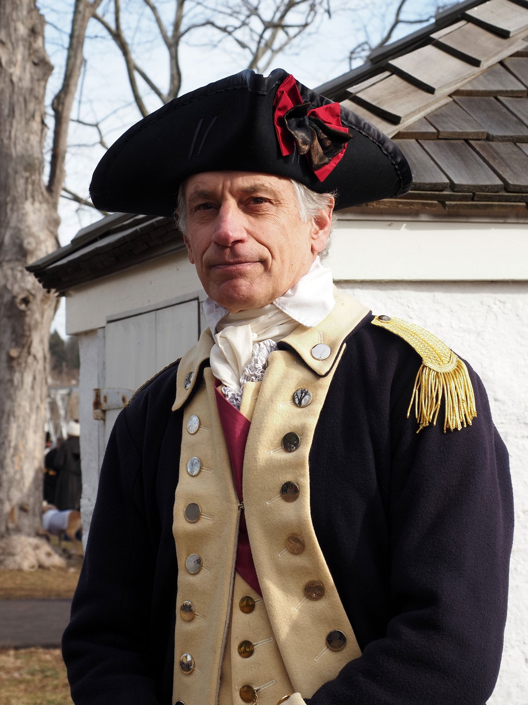 A man in colonial military attire poses outdoors, showcasing historical reenactment.