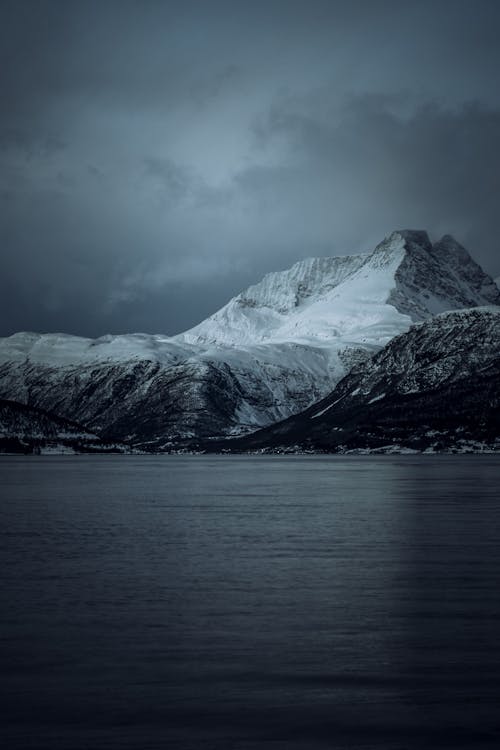 Free Snow-covered Mountain Facing Body of Water Under Heavy Clouds Stock Photo