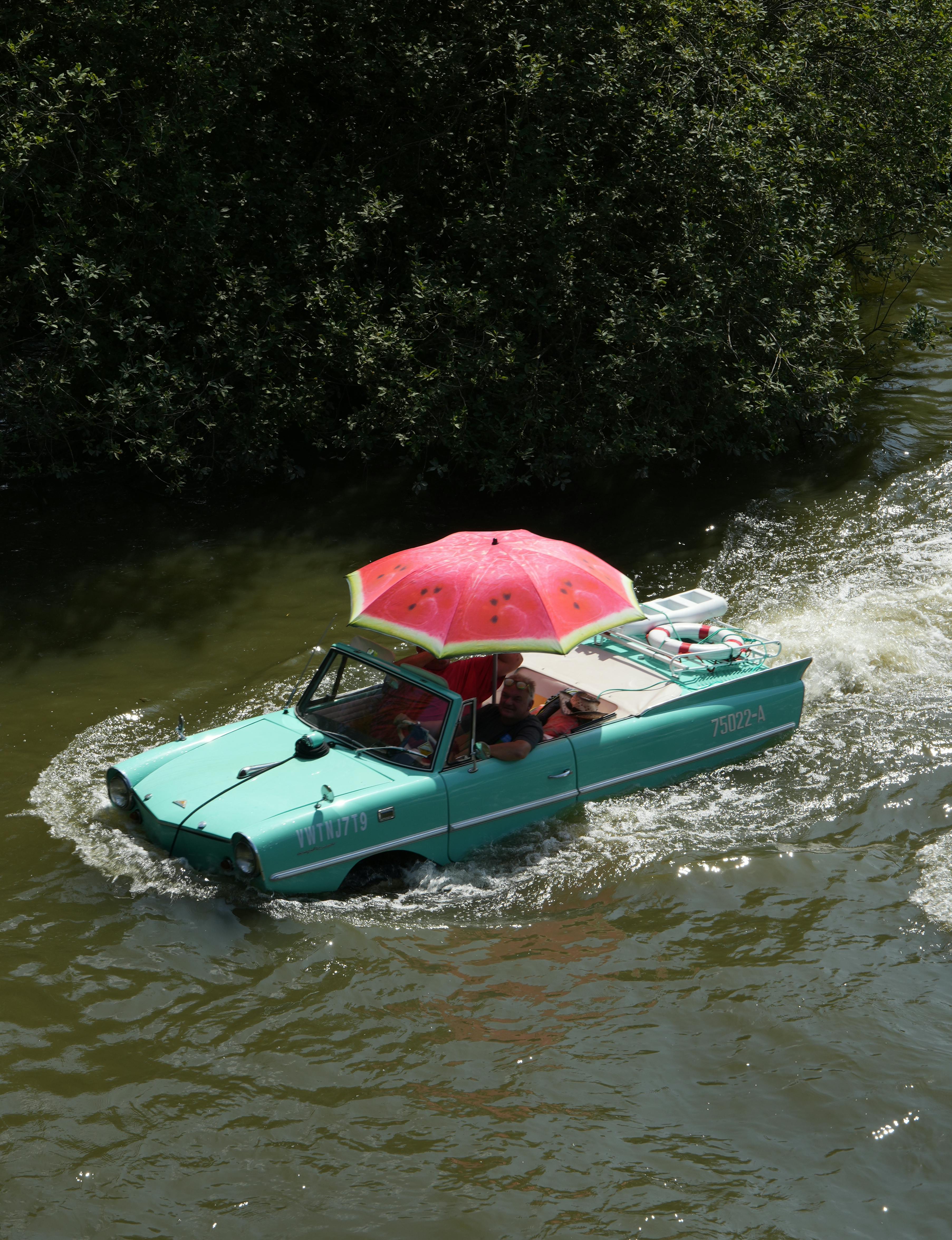 Amphibious car with umbrella floating in a scenic river.