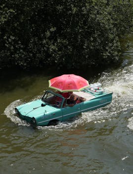 Amphibious car with umbrella floating in a scenic river.