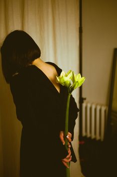 Artistic image of a woman with a lily, photographed indoors with warm tones.