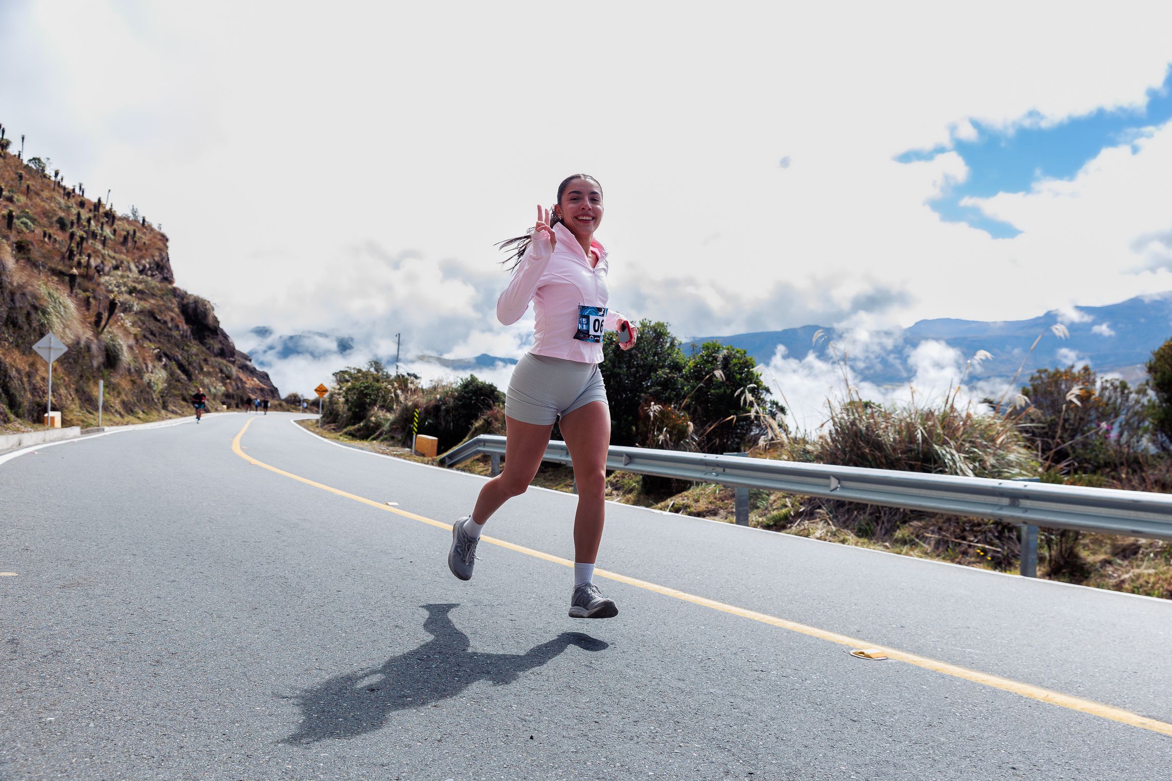 A smiling runner flashing a peace sign on a bright mountain road