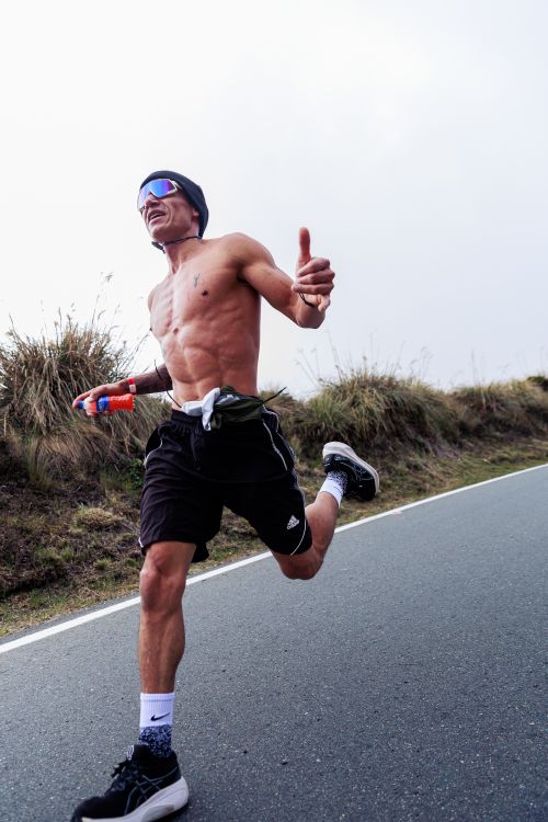 Free Shirtless man running energetically on an outdoor road in sunny weather. Stock Photo
