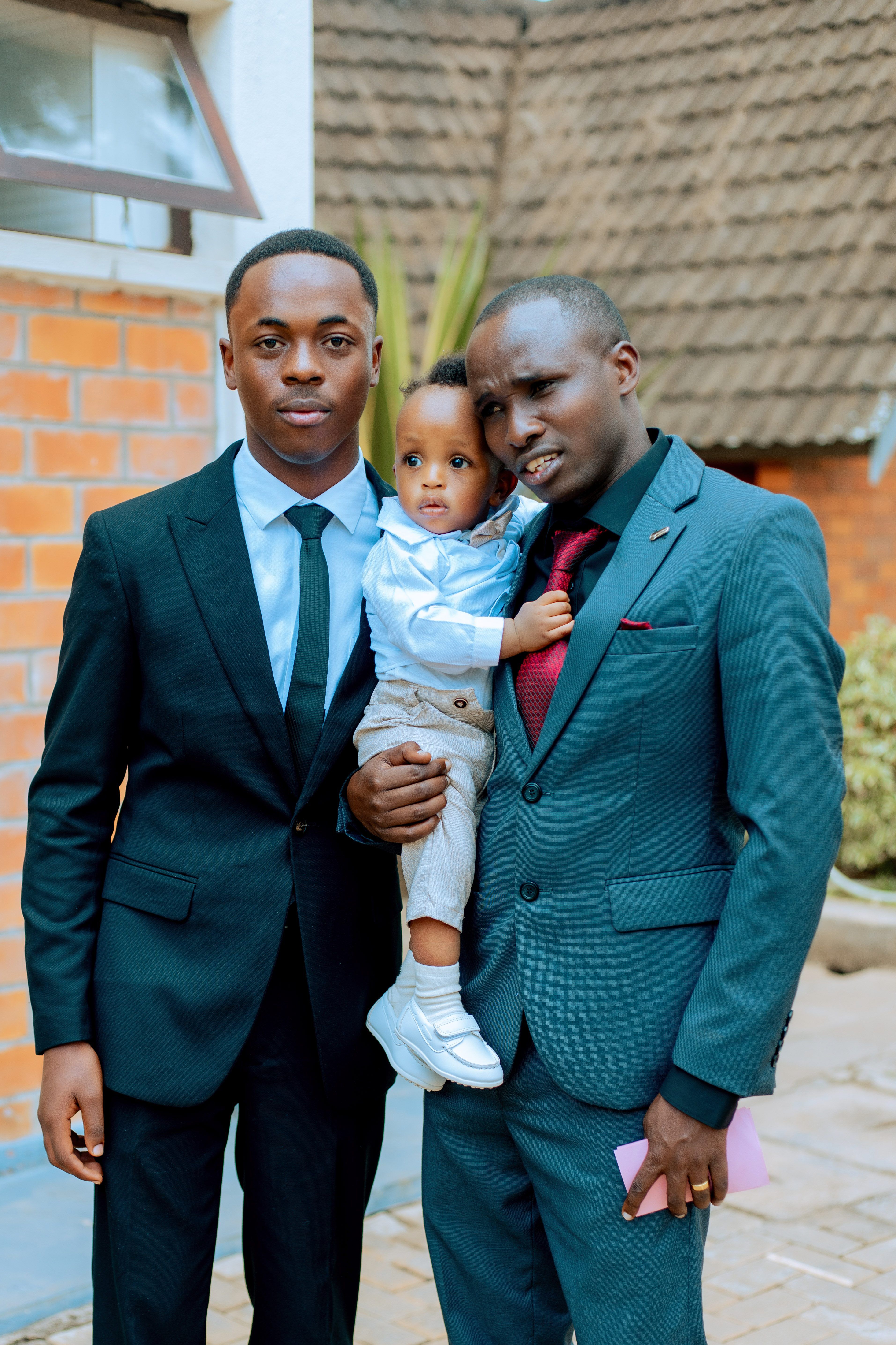 A family portrait featuring two men and a child in suits, posing outside a house.