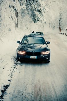 Black car navigating a snowy forest road in winter. Scenic and serene.