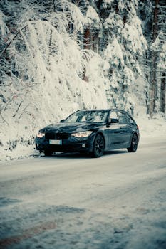 Sleek black car driving through picturesque snowy forest landscape in winter.