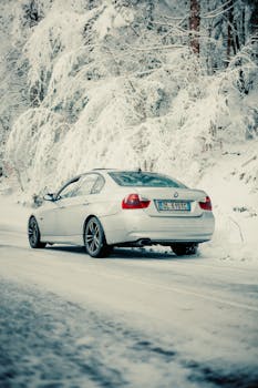 A sleek luxury car driving on a snow-covered road amid a winter wonderland.