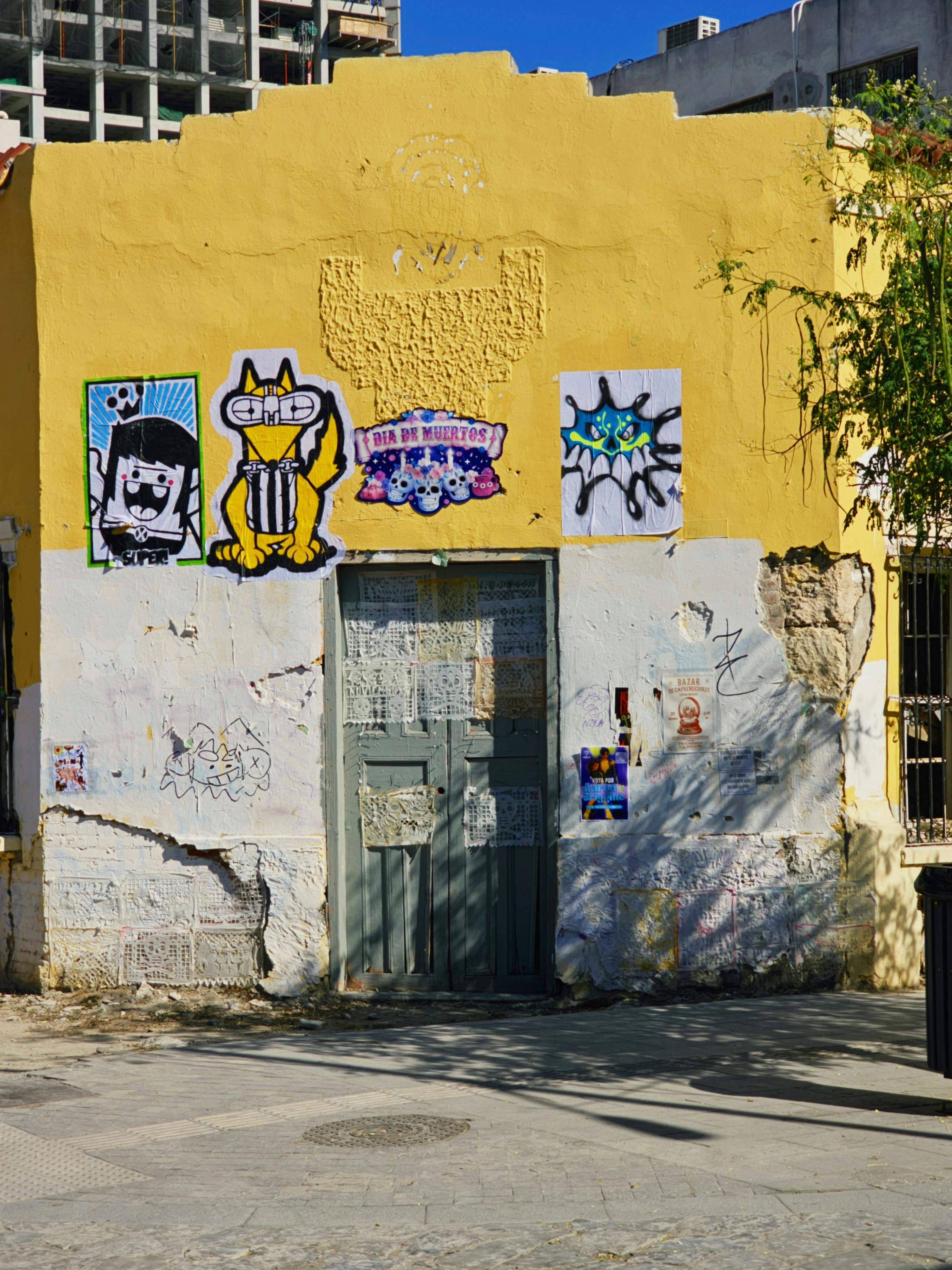 Arte callejero vibrante y carteles en la pared de un antiguo edificio urbano bajo un cielo despejado.