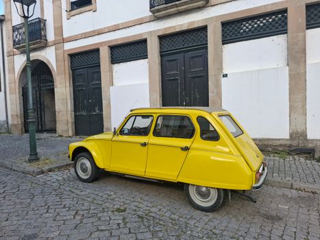 Classic yellow car parked on a cobblestone street against historic architecture