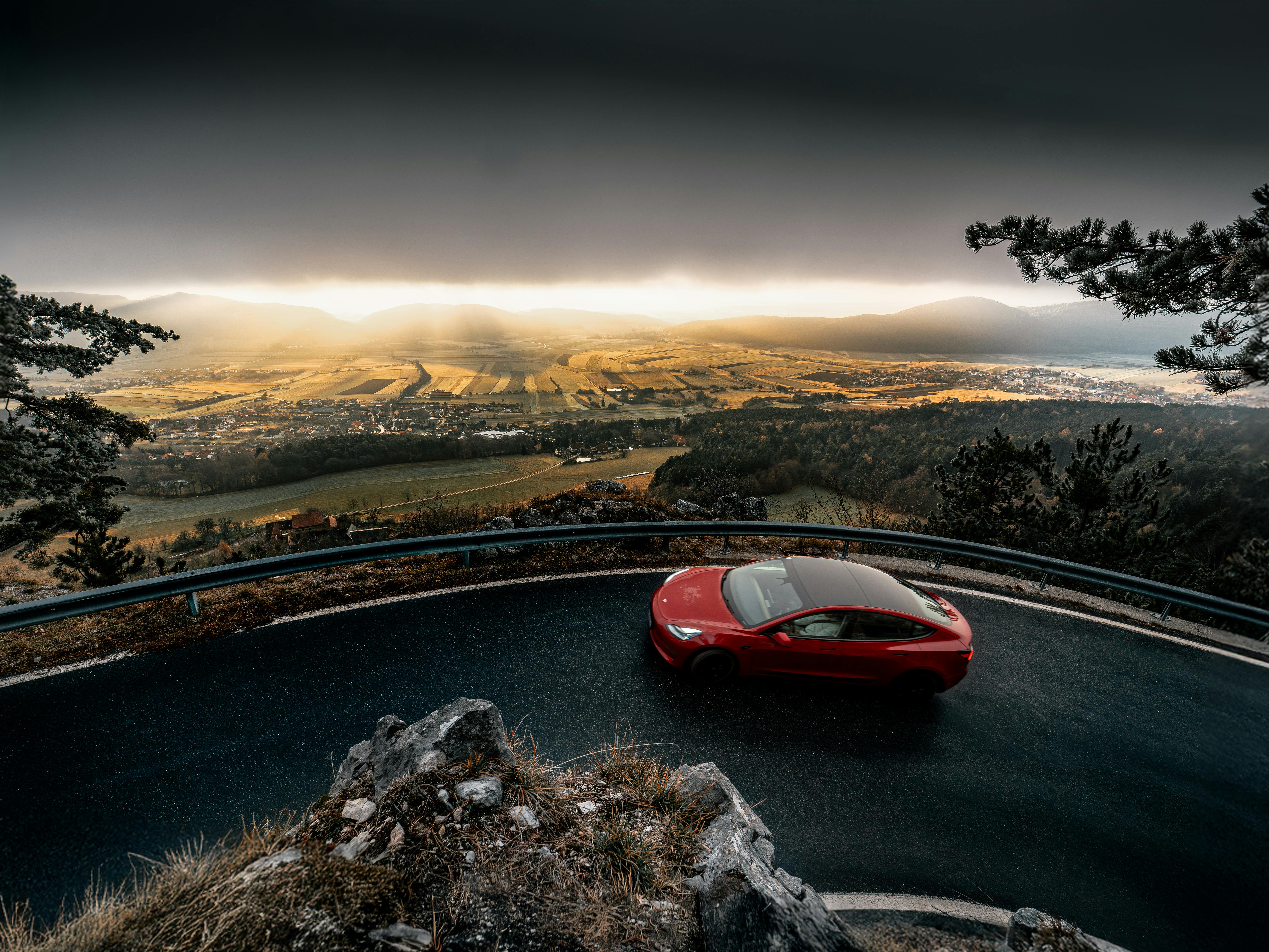Gratis Sebuah mobil merah mencolok melaju di jalan berkelok-kelok dengan pemandangan Niederösterreich, Austria yang menakjubkan. Foto Stok
